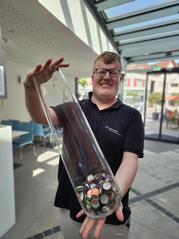 Ein Mitarbeiter des Simplex hält eine große Glasvase in der Hand, in der Kronkorken sind.