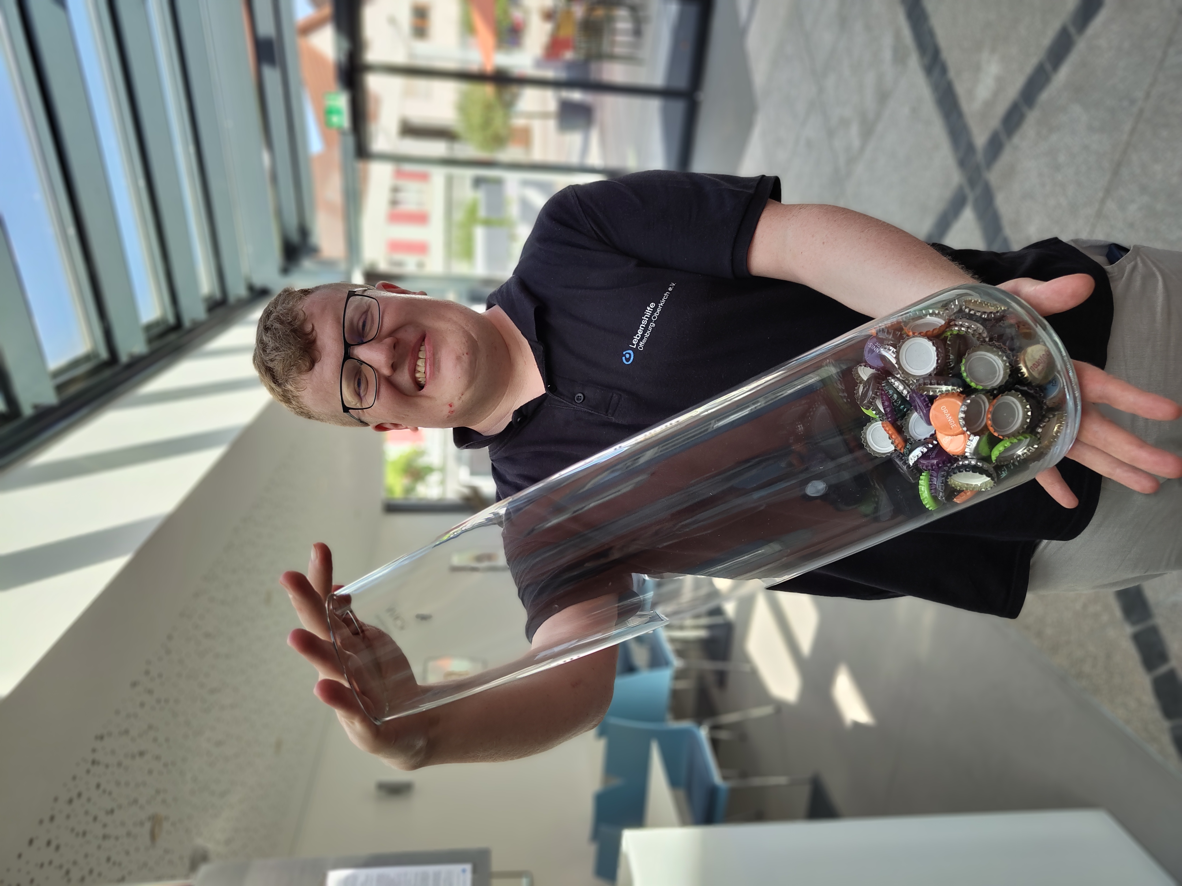 Ein Mitarbeiter des Simplex hält eine große Glasvase in der Hand, in der Kronkorken sind.