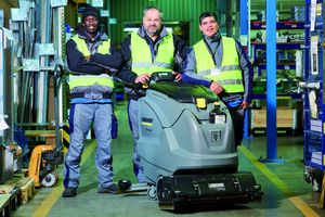 Drei Mitarbeiter mit einem Bodenreinigungsgerät in einer Werkshalle.