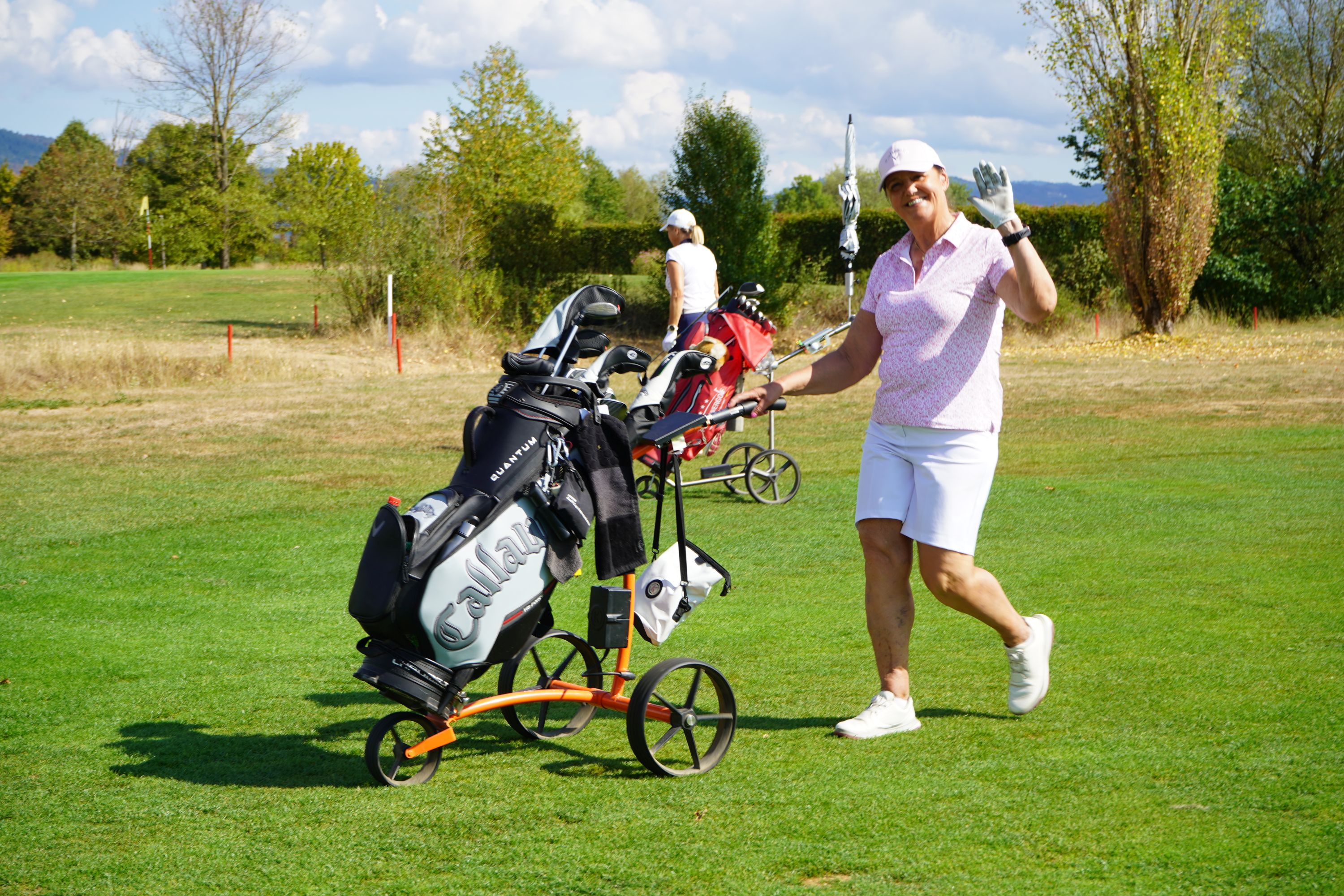 Eine Golfspielerin winkt fröhlich in Richtung Kamera.