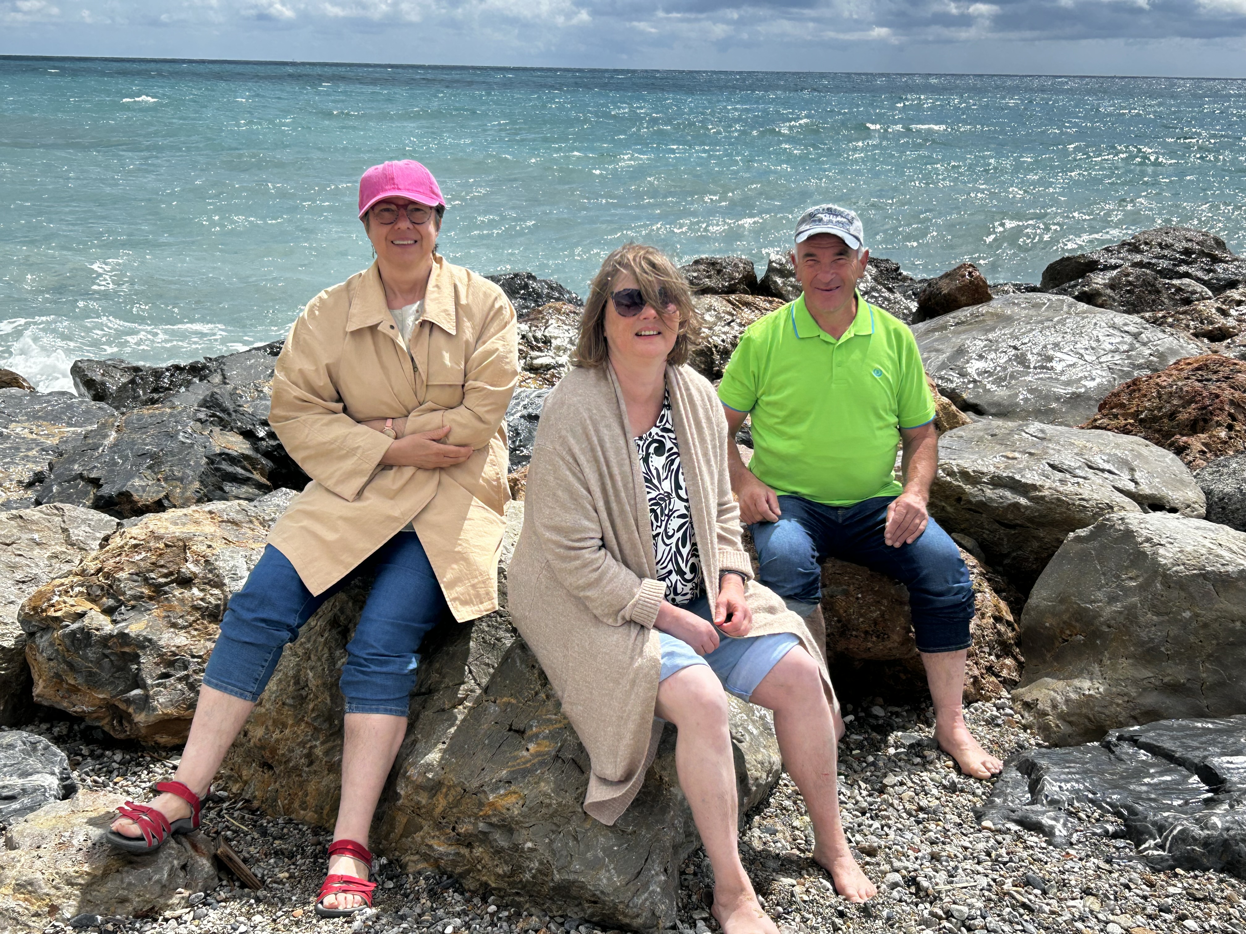 Drei Menschen mit Behinderung sitzen am Strand von Pietra Ligure.